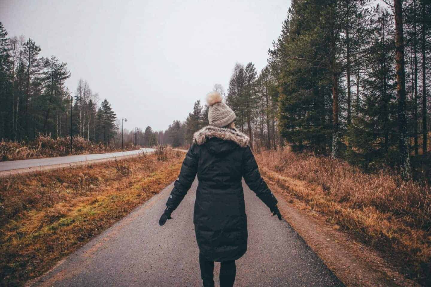 girl walking down grey and dreary lane in finland with big pine trees